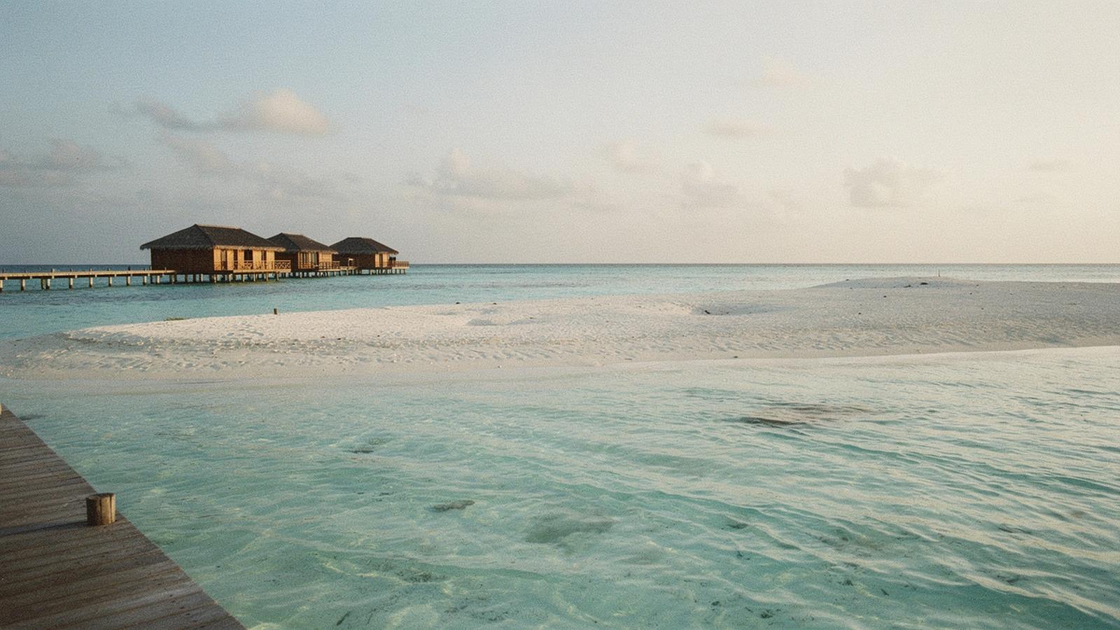 Turquoise lagoon, sandbank and overwater jetty in the Maldives in late afternoon light